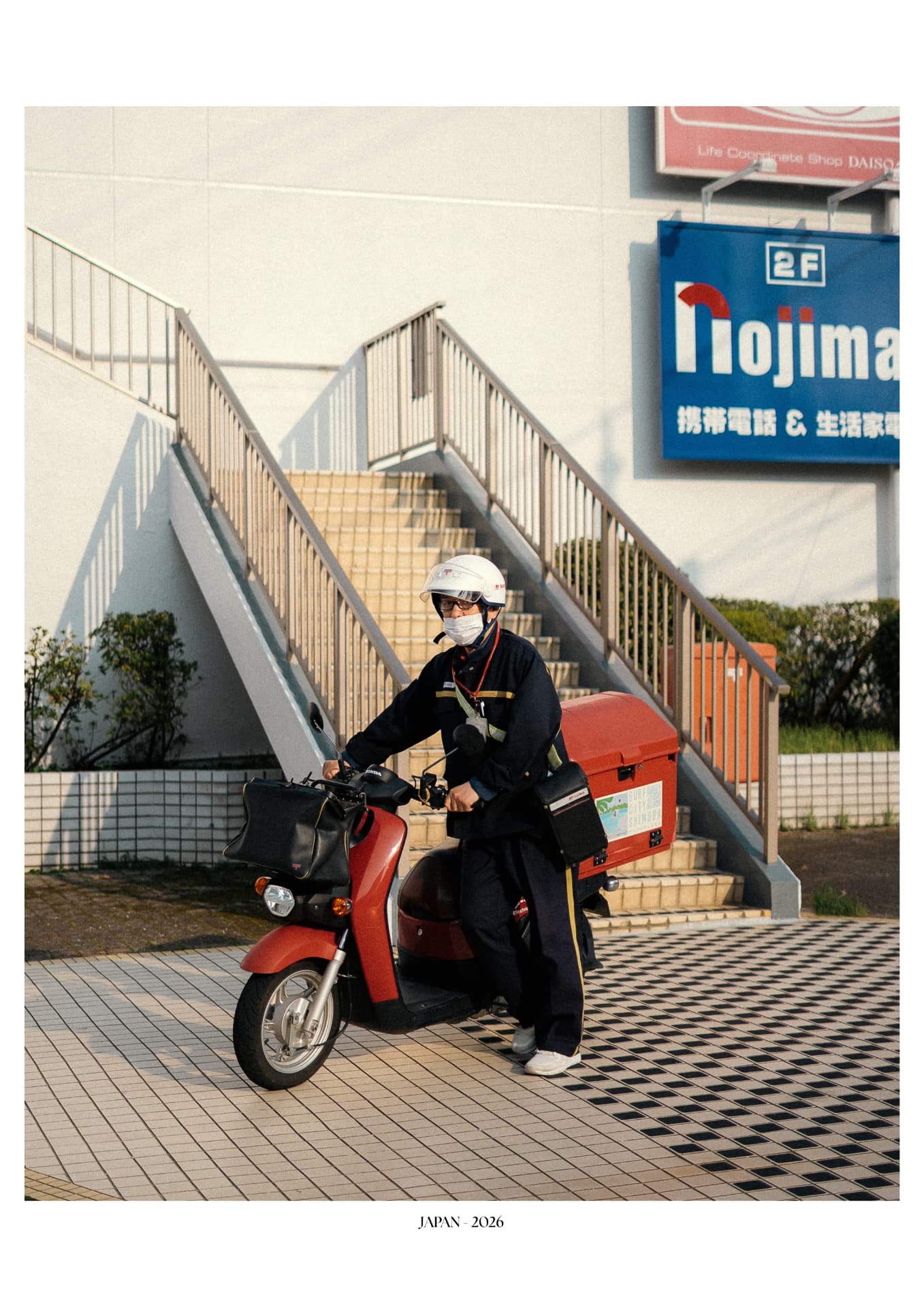 Facteur japonais sur son scooter rouge devant un escalier
